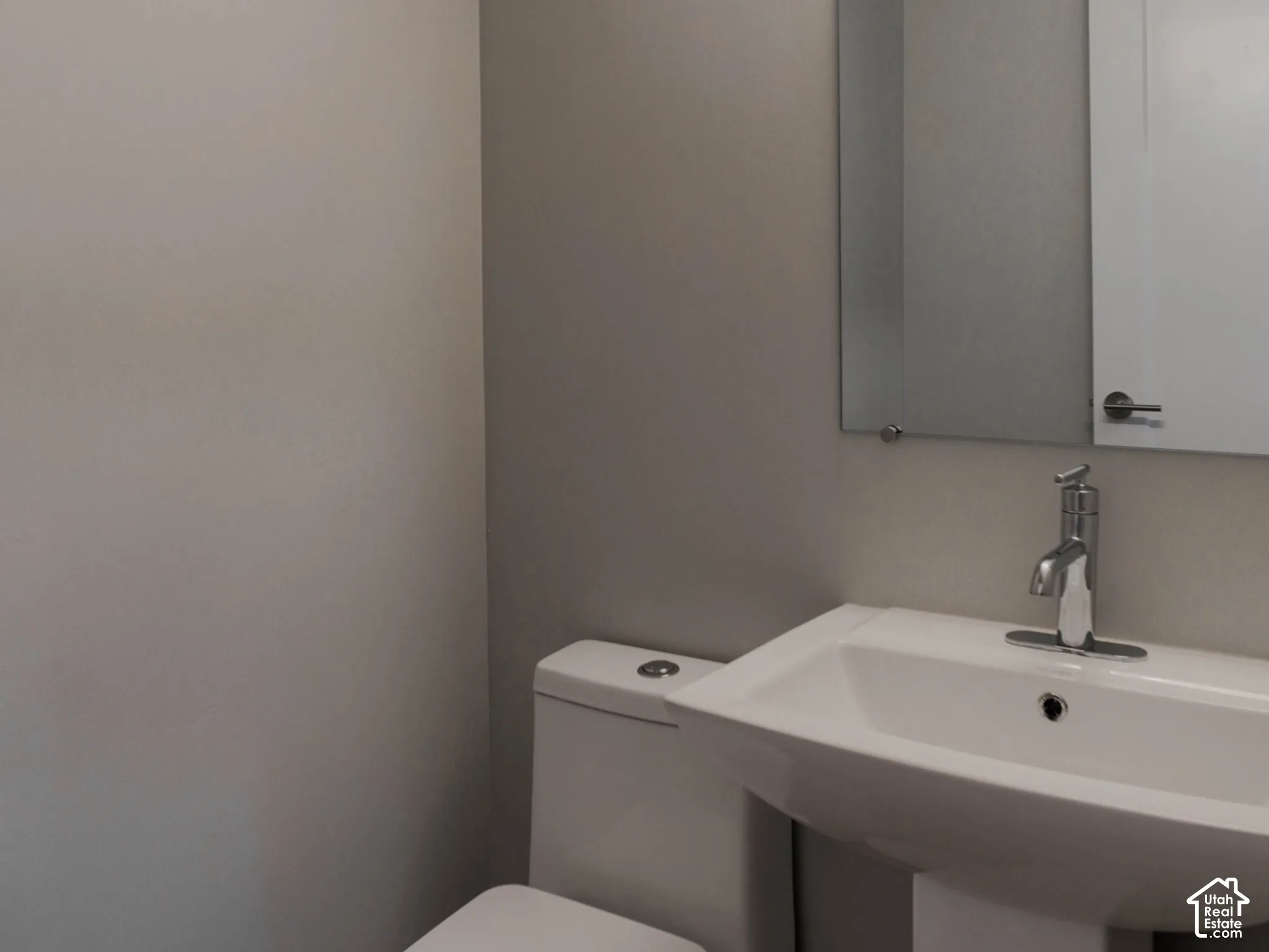 Pedestal sink with a single-handle chrome faucet, rectangular wall-mounted mirror, linear vanity light, and a high-profile white toilet