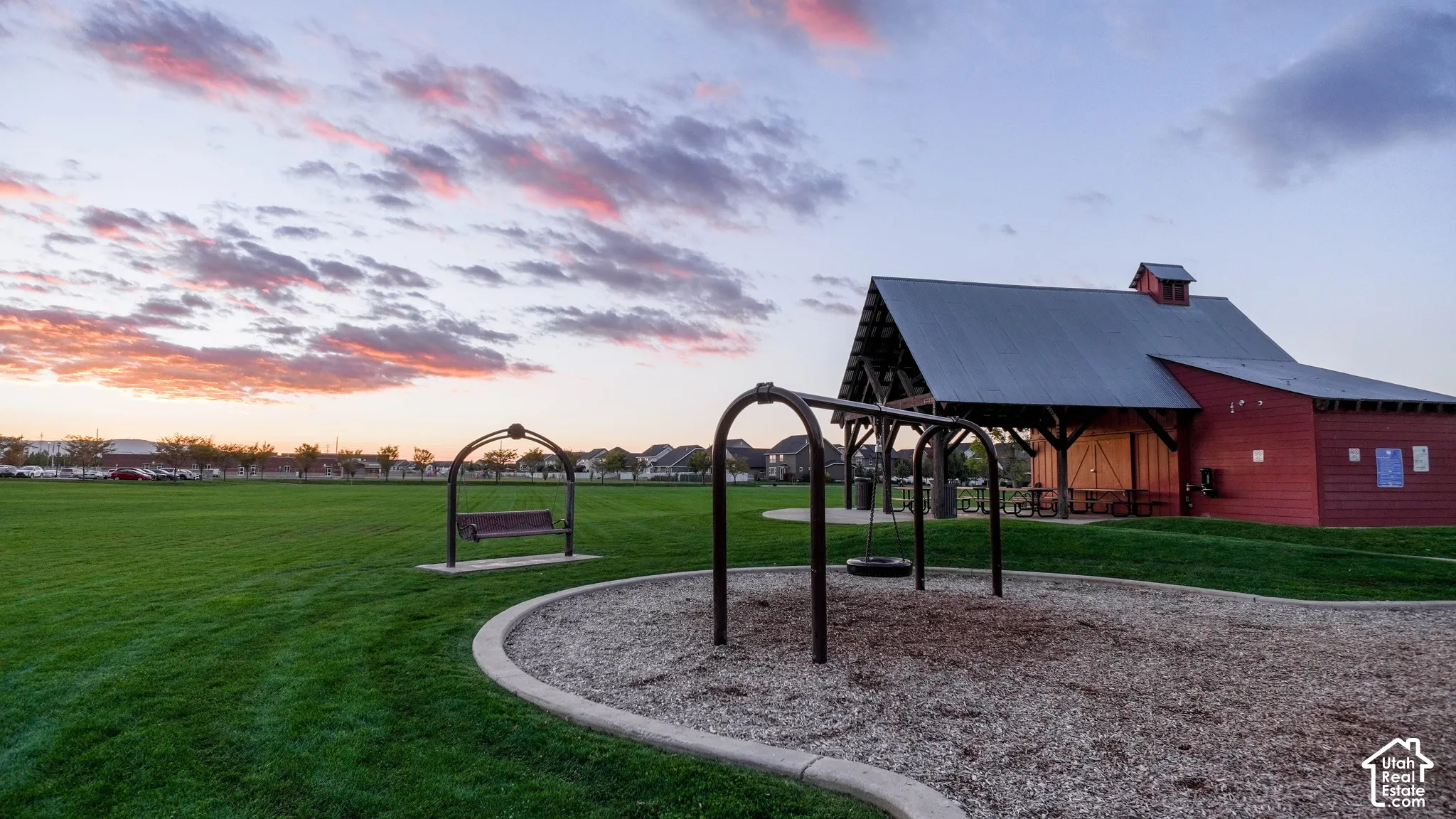 Expansive manicured lawn featuring a metal-roofed pavilion, integrated playground equipment, and decorative swing set