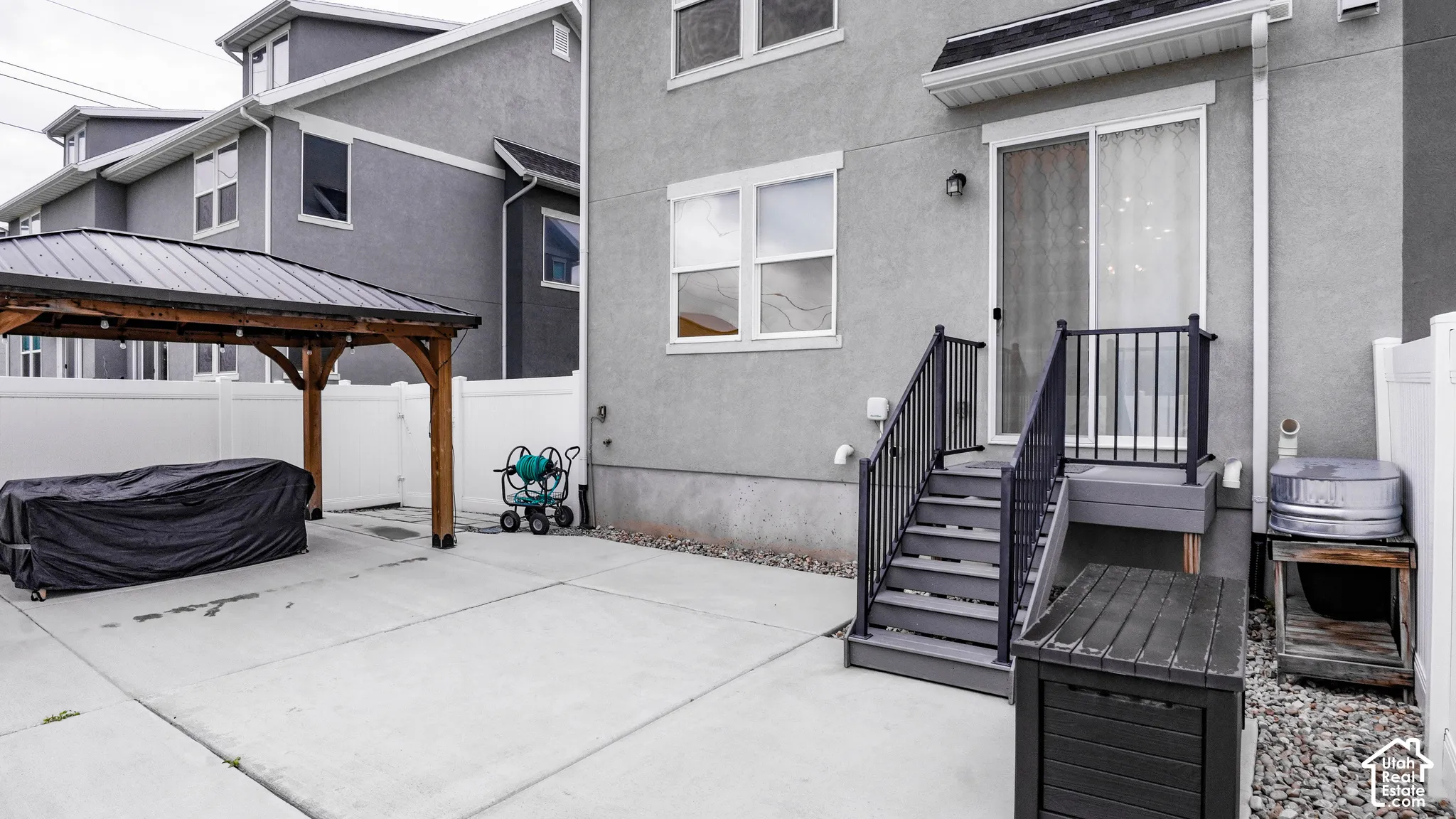 Rear exterior featuring a concrete patio, a covered pergola, sliding glass doors, stairs with metal railings, and perimeter vinyl fencing