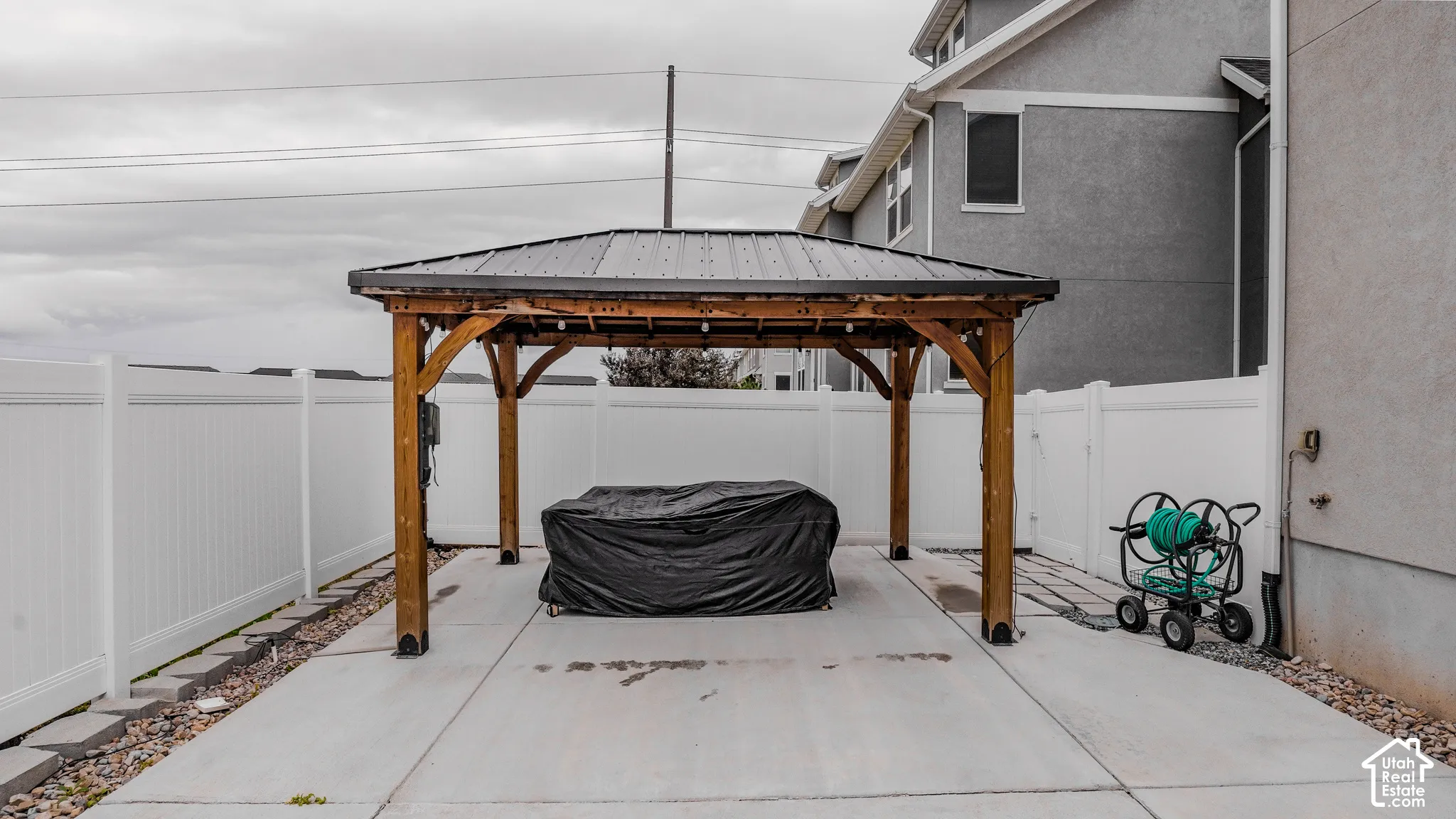 Outdoor patio area featuring a wood-frame gazebo with a metal roof, concrete slab flooring, and white vinyl privacy fencing