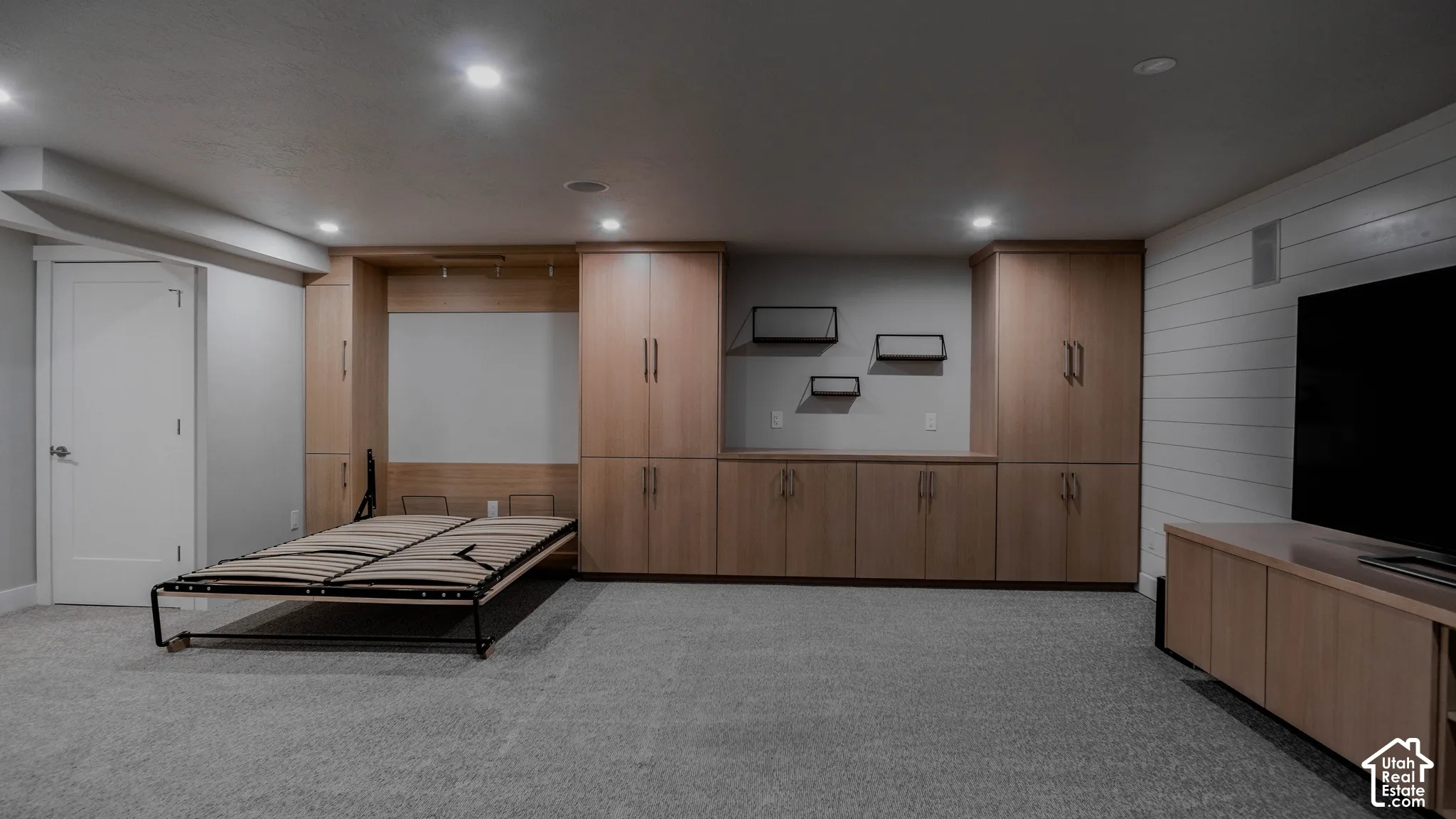 Built-in light-wood cabinetry, integrated murphy bed system, horizontal plank wall detailing, and recessed ceiling lighting