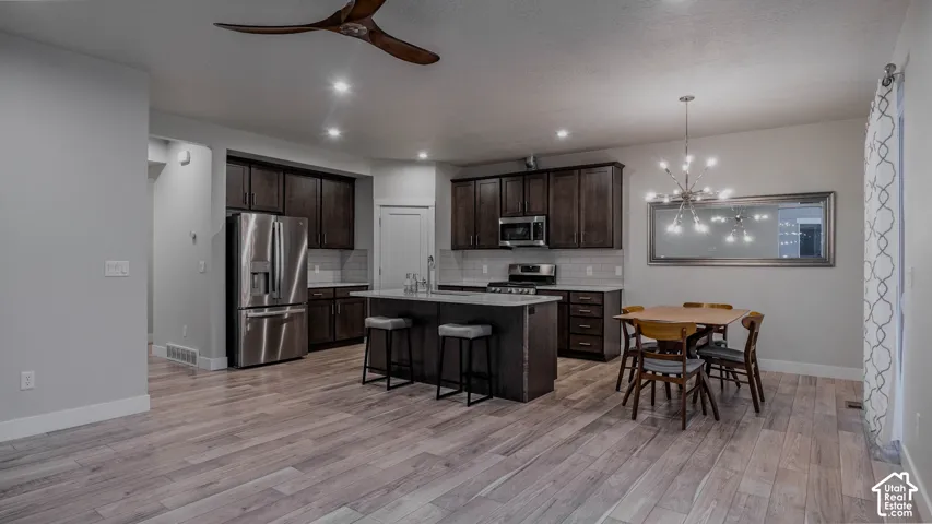 Open-concept kitchen featuring dark wood cabinetry, an island with quartz countertops, stainless steel appliances, recessed lighting, and LVP flooring
