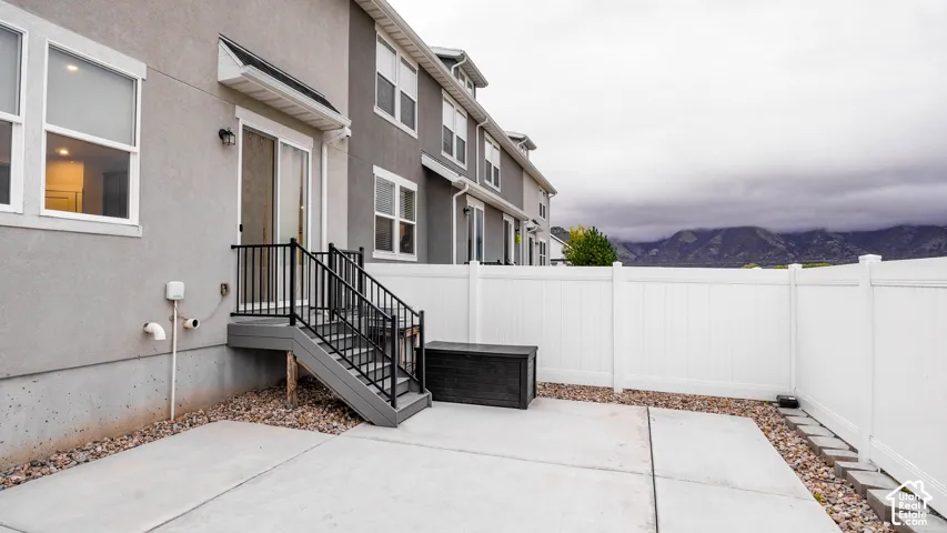 Rear exterior featuring a concrete patio, white vinyl privacy fencing, metal railing, and stairs, accented by mountain scenery