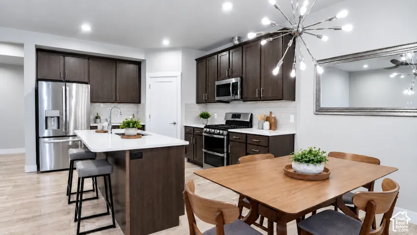 Kitchen featuring dark-finish cabinetry, quartz countertops, stainless steel appliances, a central island with an integrated sink, and LVP flooring