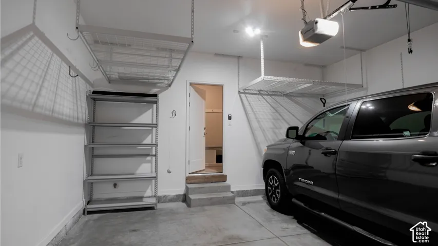 Garage space featuring two overhead storage racks, integrated metal shelving, concrete flooring, and an automated garage door opener