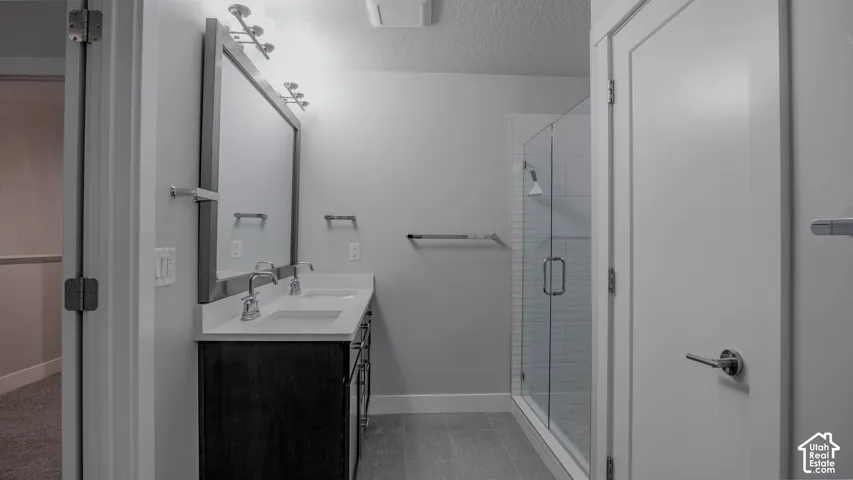 Dual-sink vanity with a quartz countertop, full-width framed mirror, glass-enclosed shower with subway tile surround, and tile flooring