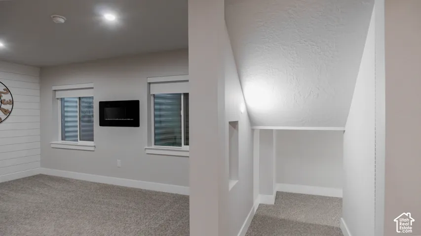 Horizontal shiplap accent wall, wall-mounted electric fireplace, recessed ceiling lighting, and custom under-stair storage nook with carpeted flooring