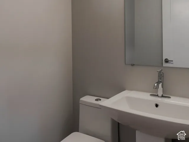 Pedestal sink with a single-handle chrome faucet, rectangular wall-mounted mirror, linear vanity light, and a high-profile white toilet