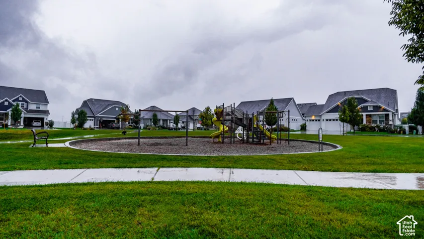 Community common area featuring a playground structure, manicured lawn, concrete walking path, and metal bench seating