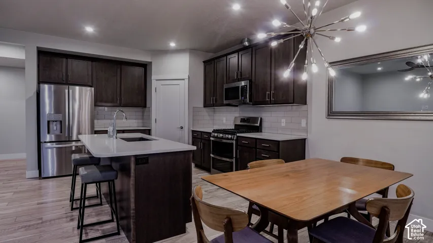 Kitchen featuring dark-finish cabinetry, central island with quartz countertops, subway tile backsplash, stainless steel appliances, and LVP flooring