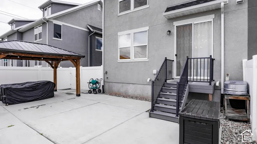 Rear exterior featuring a concrete patio, a covered pergola, sliding glass doors, stairs with metal railings, and perimeter vinyl fencing