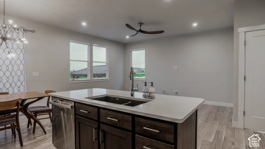 Kitchen island featuring quartz countertops, dark-stained cabinetry, a stainless steel undermount sink with a gooseneck faucet, and wood-finish flooring