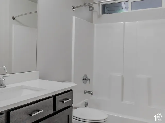 Bathroom featuring a dark wood-finish vanity with a quartz countertop, patterned tile flooring, a large wall-mounted mirror, and a tub-shower combination with a transom window