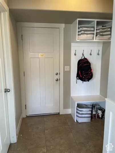 Entryway featuring tile flooring, a white paneled door, and built-in white cabinetry with a beadboard accent, integrated wall hooks, and overhead storage compartments