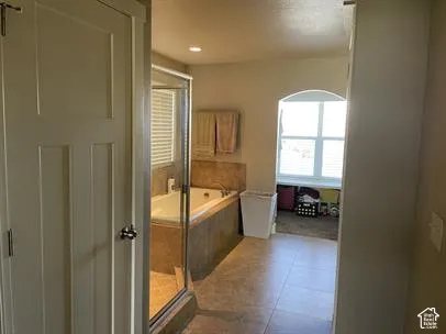 Bathroom featuring tile flooring, a soaking tub with tile surround, a glass-enclosed shower, and an arched window