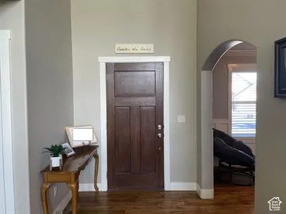 Solid wood-finish front door with a multi-panel design, set within a neutral-toned foyer featuring wood-finish flooring and an arched architectural opening