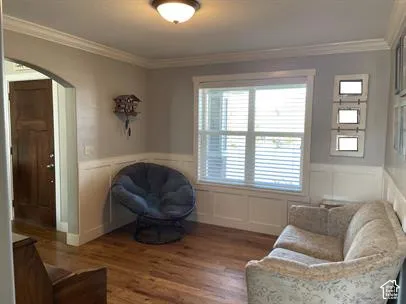 Wood-finish flooring, white wainscoting, arched entryway, and crown molding