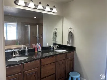 Dual-sink vanity with dark stone countertops, wood-finish cabinetry, a large wall-mounted mirror, and multi-bulb vanity lighting