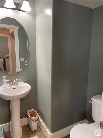 Pedestal sink with a dual-handle faucet, oval wall-mounted mirror, two-light fixture, and ceramic toilet