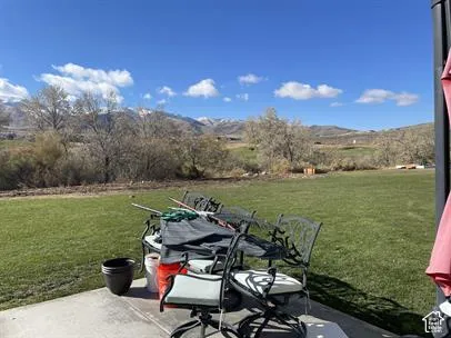 Concrete patio overlooking an expansive grass lawn with a backdrop of snow-capped mountains and mature trees