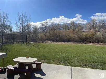 Backyard featuring a concrete patio, a manicured lawn, metal perimeter fencing, and a mountain backdrop
