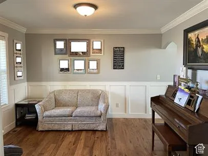 Wood-finish flooring, half-wall wainscoting, crown molding, and an arched entry