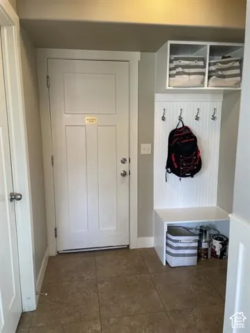 Entryway featuring tile flooring, a white paneled door, and built-in white cabinetry with a beadboard accent, integrated wall hooks, and overhead storage compartments