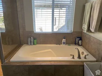 Built-in soaking tub with a tile surround, glass-enclosed shower, and window with integrated blinds