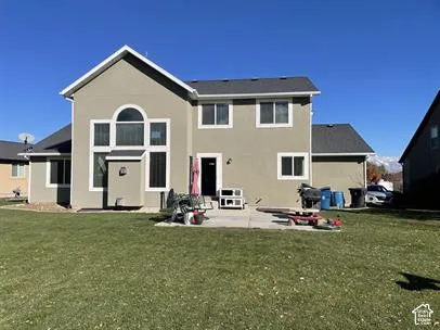 Two-story residence featuring a concrete patio, stucco siding, multi-pane windows with a large arched transom, and an expansive lawn