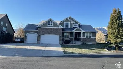 Multi-level residence featuring a stone and siding exterior, multiple roof gables, a three-car garage, and concrete driveway
