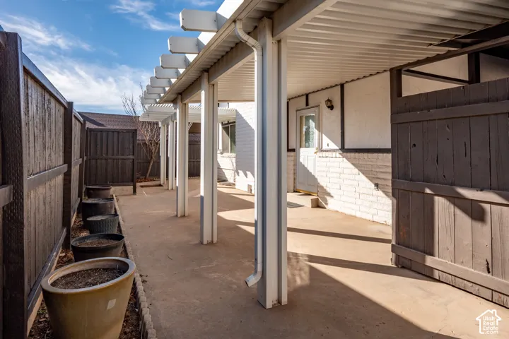 Covered patio featuring a painted brick exterior, pergola-style roofing, and privacy fencing