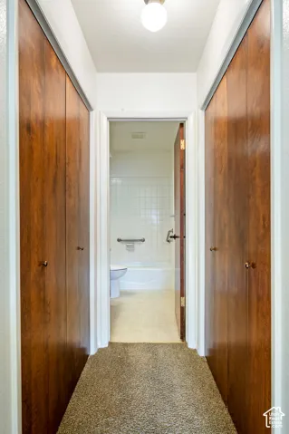 Hallway featuring dual floor-to-ceiling wood-finish bifold closet doors, carpeting, and a flush-mount ceiling light
