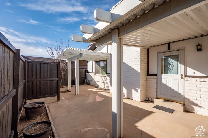 Exterior patio featuring a concrete surface, overhead pergola structure, white painted brick siding, and an opaque glass-panel entry door