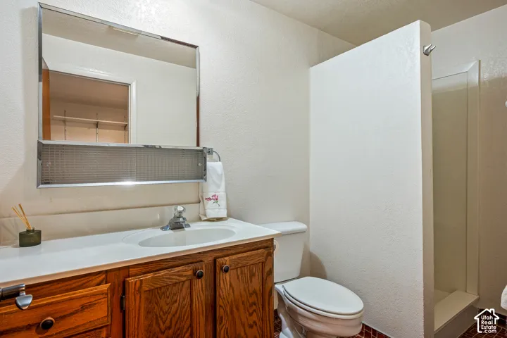 Bathroom featuring a vanity with wood-finish cabinetry, integrated oval sink, chrome-finish faucet, and a large wall-mounted mirror with an integrated shelf