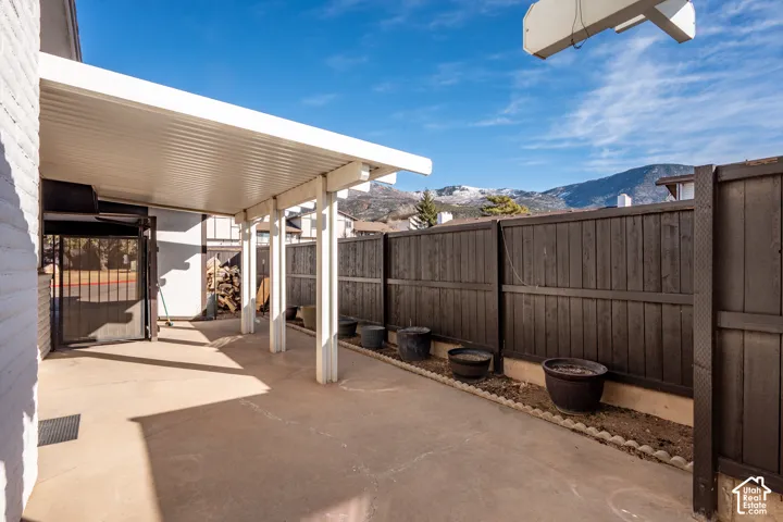 Covered concrete patio featuring a solid roof structure, painted dark wood privacy fencing, and mountain backdrop