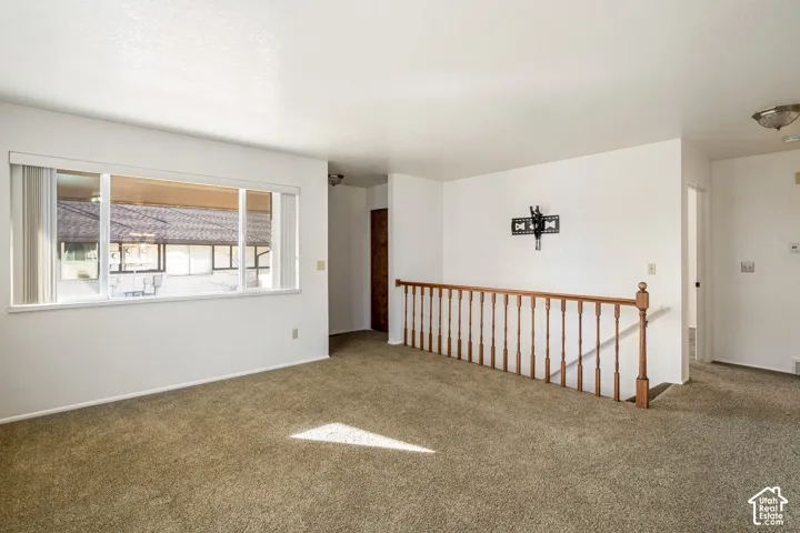 Large interior space featuring wall-to-wall carpeting, expansive window, and wood-finish railing with vertical balusters