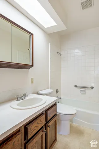 Bathroom featuring a skylight, vanity with a solid-surface countertop and integrated sink, recessed medicine cabinet, and a tiled tub surround with a mounted grab bar