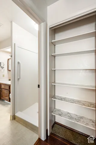 Walk-in shower featuring a white surround and a fixed safety grab bar, complemented by built-in shelving with stone-finish surfaces
