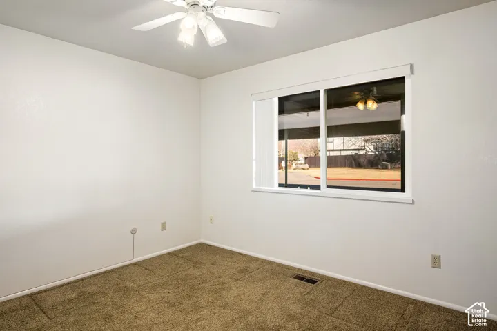 Neutral interior featuring textured wall finishes, wall-to-wall carpeting, a large sliding window with blinds, and a white ceiling fan with integrated lighting