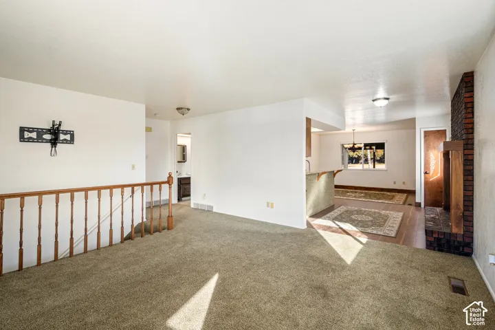 Open interior space featuring a floor-to-ceiling brick fireplace, wood-finish staircase railing, and neutral wall-to-wall carpeting