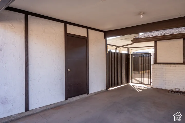 Covered carport featuring textured wall finishes, timber-framing accents, an integrated storage closet, and a metal security gate