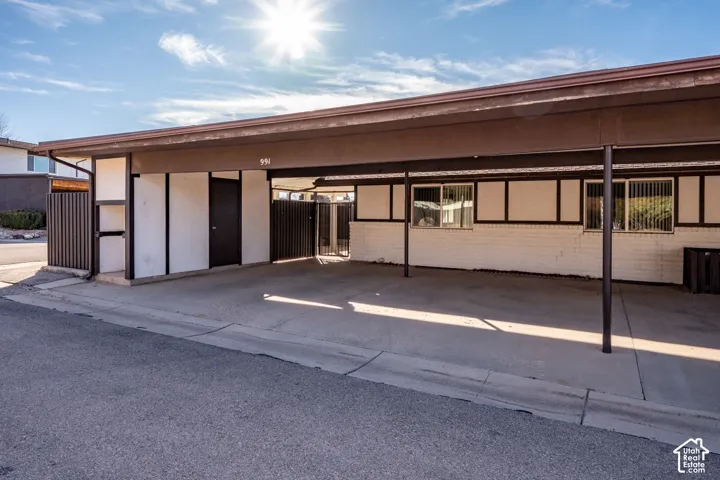 Covered carport featuring a concrete pad, painted brick exterior, metal fencing, and sliding windows
