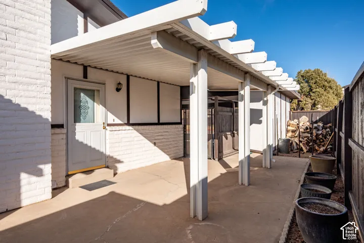 Exterior patio featuring a covered pergola, white-painted brick facade, and a single-entry door with glass detailing
