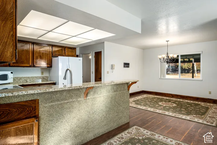 Kitchen featuring wood cabinetry, stone-surfaced breakfast bar, recessed tray ceiling lighting, and wood-finish flooring