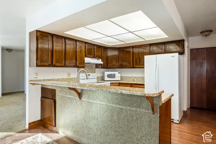 Kitchen featuring wood cabinetry, stone-finish countertops, an integrated breakfast bar, recessed lighting, and wood-finish flooring