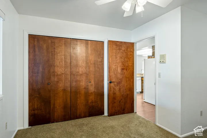Room interior featuring wood-finish bi-fold closet doors, a matching wood-finish entry door, neutral-toned carpeting, and a ceiling fan with integrated lighting