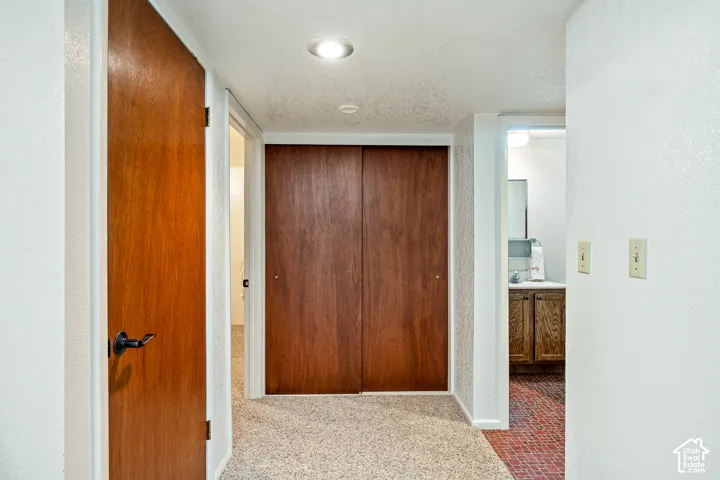 Interior hallway featuring solid wood-finish doors, built-in floor-to-ceiling sliding closet, recessed lighting, and neutral carpeted flooring
