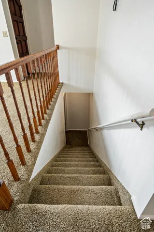 Staircase featuring carpeted steps, a wood-finish railing with vertical balusters, and a wall-mounted metal handrail