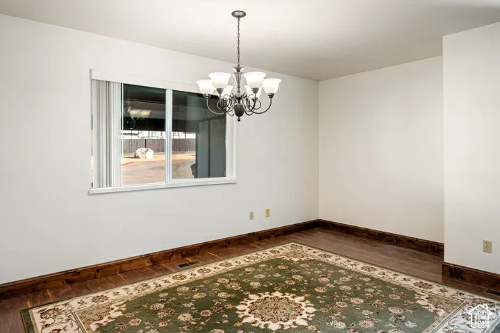Room featuring wood-finish flooring, dark wood-tone molding, a sliding window with white framing, and a six-light chandelier with a metallic finish