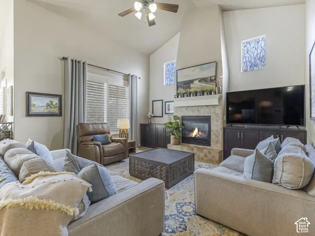 Vaulted ceilings featuring a central ceiling fan, fireplace with stone-tile surround, built-in cabinetry, and dual windows